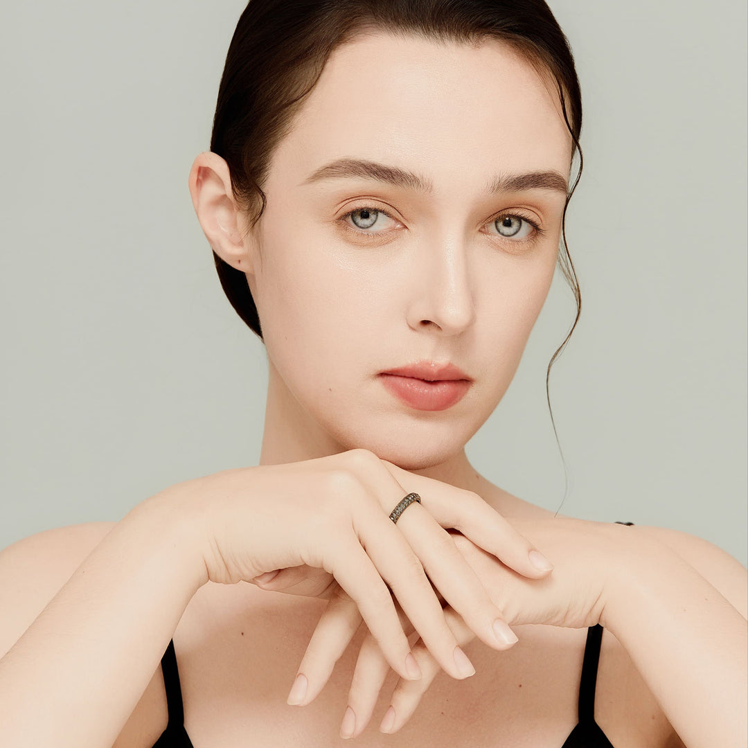 Close-up of model’s hand wearing black pavé eternity ring; detailed metalwork and strong presence.