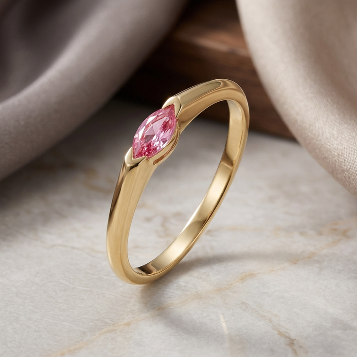 Gold ring with a pink gemstone on a marble surface