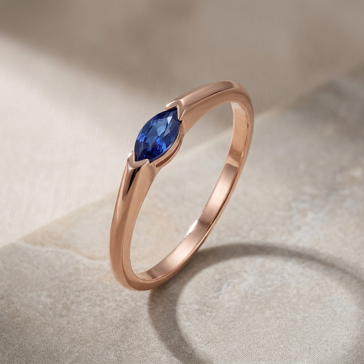 Rose gold ring with a blue gemstone on a textured beige surface